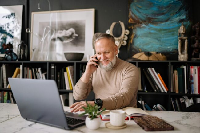 An elderly man working on his laptop while having a phone call